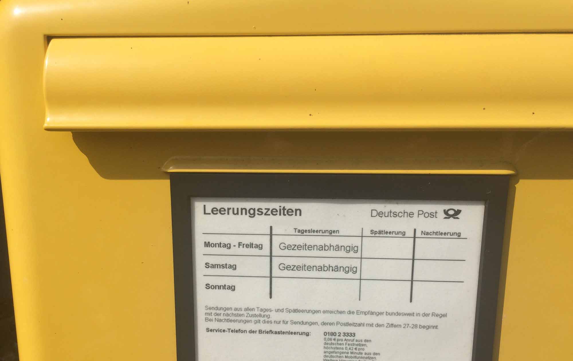 gelber Briefkasten der Post mit dem Hinweisschild, dass die Leerung gezeitenabhängig erfolgt.